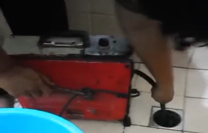 Teknisi melancarkan floor drain mampet dengan mesin spiral